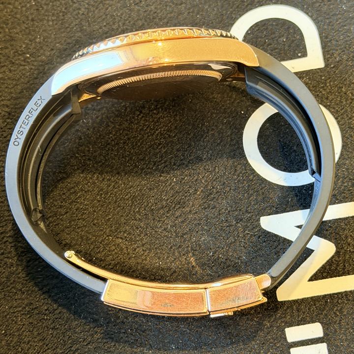 Side view of a rose gold Rolex on a black Oysterflex bracelet with Oysterflex printed on the inside